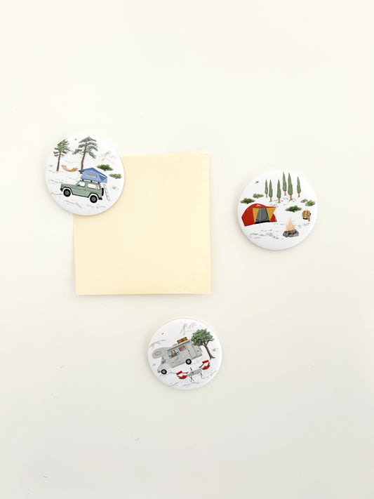 3 runde Magnete mit Campingmotiven an einer Magnetwand. Die großen Magnete Buttons zeigen Wohnmobil, Zelt und Jeep mit Dachzelt