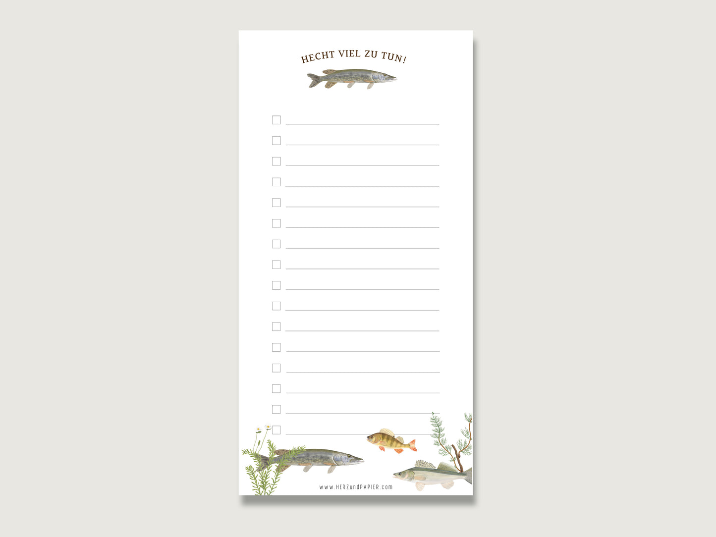 Stilvolles und lustiges Geschenk fürs Büro: Ein hochformatiger Notizblock im Format DIN Lang aus weißem Naturpapier mit einer Reihe von quadratischen Checkboxen zum Abhaken auf der linken Seite. Unten befindet sich die detaillierte Handillustration eines Hechts sowie der braune, geschwungene Schriftzug Hecht viel zu tun!. Der Block liegt mittig auf einer schlichten, hellen Fläche.  