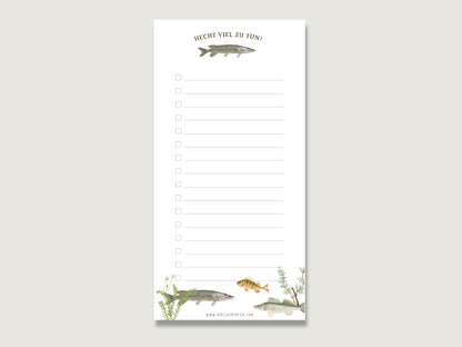 Stilvolles und lustiges Geschenk fürs Büro: Ein hochformatiger Notizblock im Format DIN Lang aus weißem Naturpapier mit einer Reihe von quadratischen Checkboxen zum Abhaken auf der linken Seite. Unten befindet sich die detaillierte Handillustration eines Hechts sowie der braune, geschwungene Schriftzug Hecht viel zu tun!. Der Block liegt mittig auf einer schlichten, hellen Fläche.  