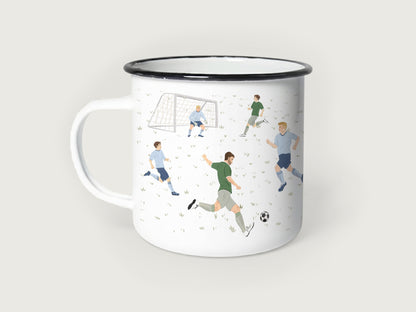 Weißer Emaillebecher mit schwarzem Rand, bedruckt mit einer handgemalten Fußball-Spielszene auf einem feinen Rasenmuster. Zu sehen sind mehrere Fußballspieler in grünen und hellblauen Trikots, ein Torwart im Fußballtor und ein klassischer Fußball beim Torschuss.
