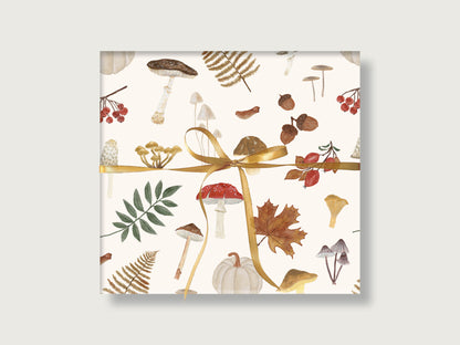 Eingepacktes Geschenk mit mattem Geschenkpapier im herbstlichen Waldmotiv aus Pilzen, Eicheln, Farnen und hellem Kürbis, gebunden mit einer goldenen Schleife.