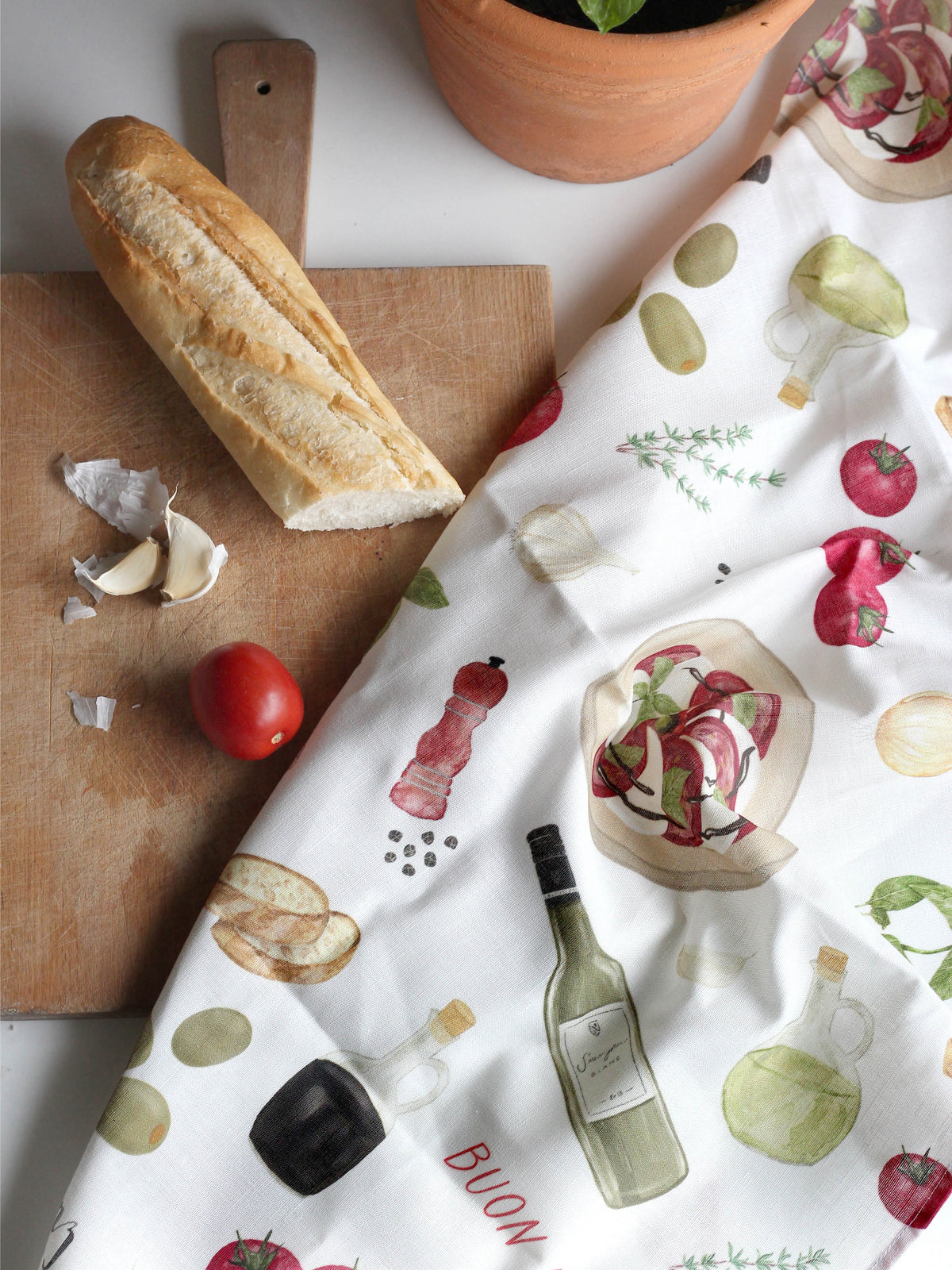 Italienisches Geschirrtuch aus saugstarken Halbleinen neben einem Schneidbrett mit Baguette, Knpblauch und Tomaten. 