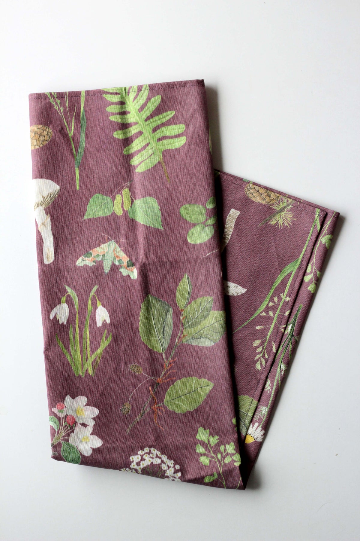 Gefaltetes Geschirrtuch aus Leinenmix mit botanischem Pflanzen- bzw. Naturmotiv auf mauve-farbenem hintergrund.