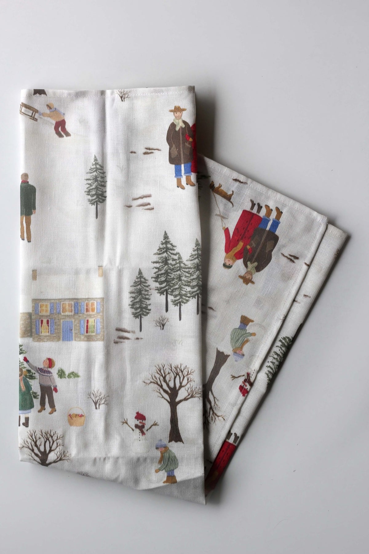 Gefaltetes Geschirrtuch mit weihnachtlichem, handgemaltem Motiv von einer Schneelandschaft, Menschen und winterlichen Szenen.