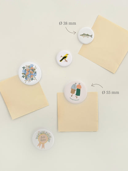 Magnetwand mit verschiedenen runden Magnet-Buttons mit handillustrierten Motiven. Zu sehen sind Motive mit Blumen, besten Freunden und für die beste Mama. Die Magnete sind weiß und rund mit Motiv.