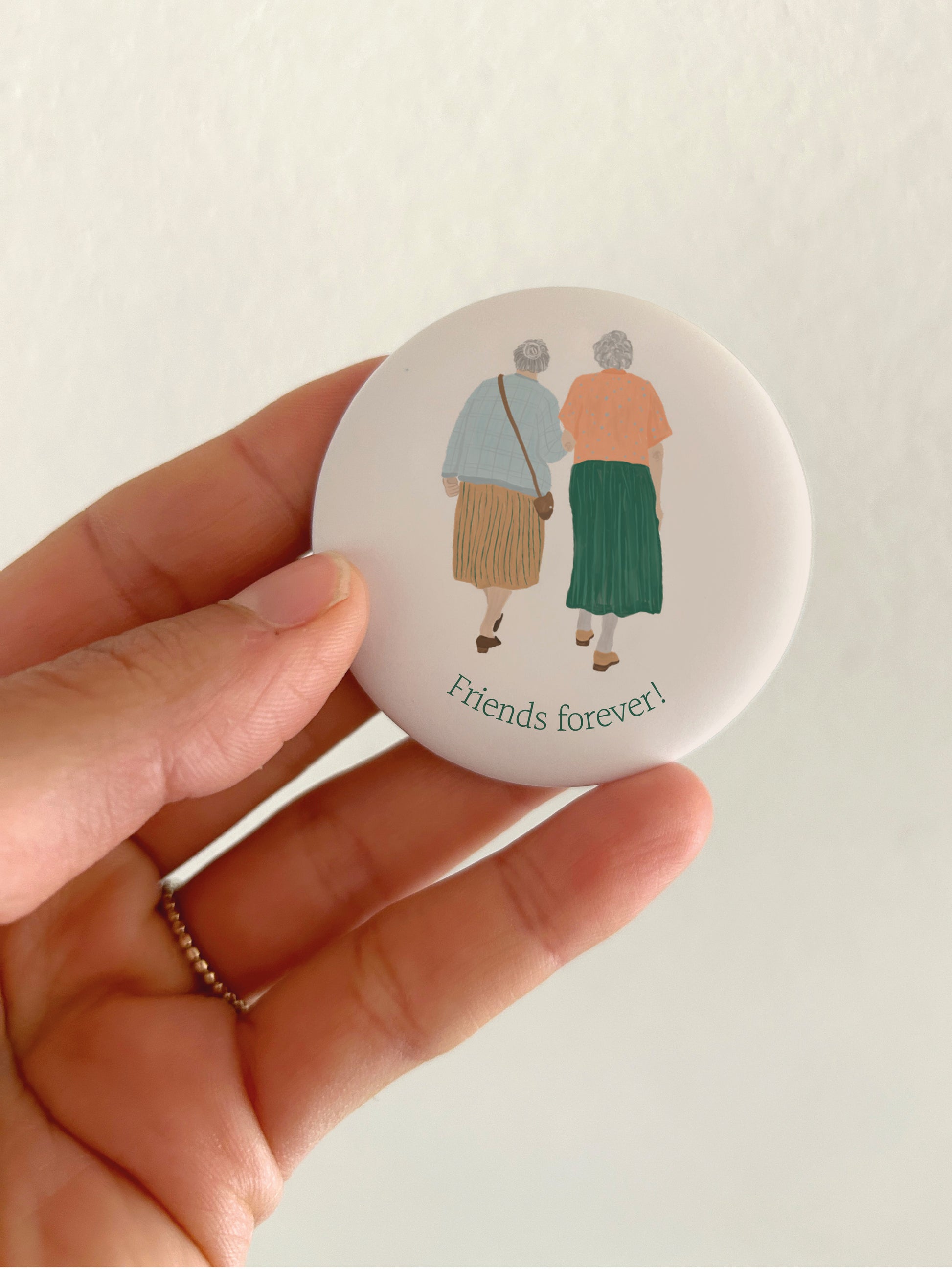 Großer Spruch-Magnet Friends forever mit 55mm Durchmesser als liebevolles Geschenk für Frauen und Freundinnen. Eine Hand hält den runden, matten Kühlschrankmagneten vor einer hellen Zimmerwand, um das spiegelungsfreie Schutzlaminat sowie die genaue Produktgröße im Alltag anschaulich zu demonstrieren.