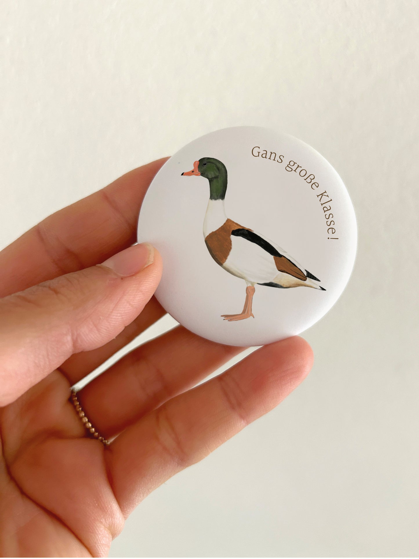 Großer Motivations-Magnet Gans große Klasse mit 55mm Durchmesser als witzige Deko für das Whiteboard oder die Magnetwand im Büro. Eine Hand hält den runden, matten Kühlschrankmagneten vor einer hellen Wand, um die reale Produktgröße und das kratzfeste Schutzlaminat zu zeigen.