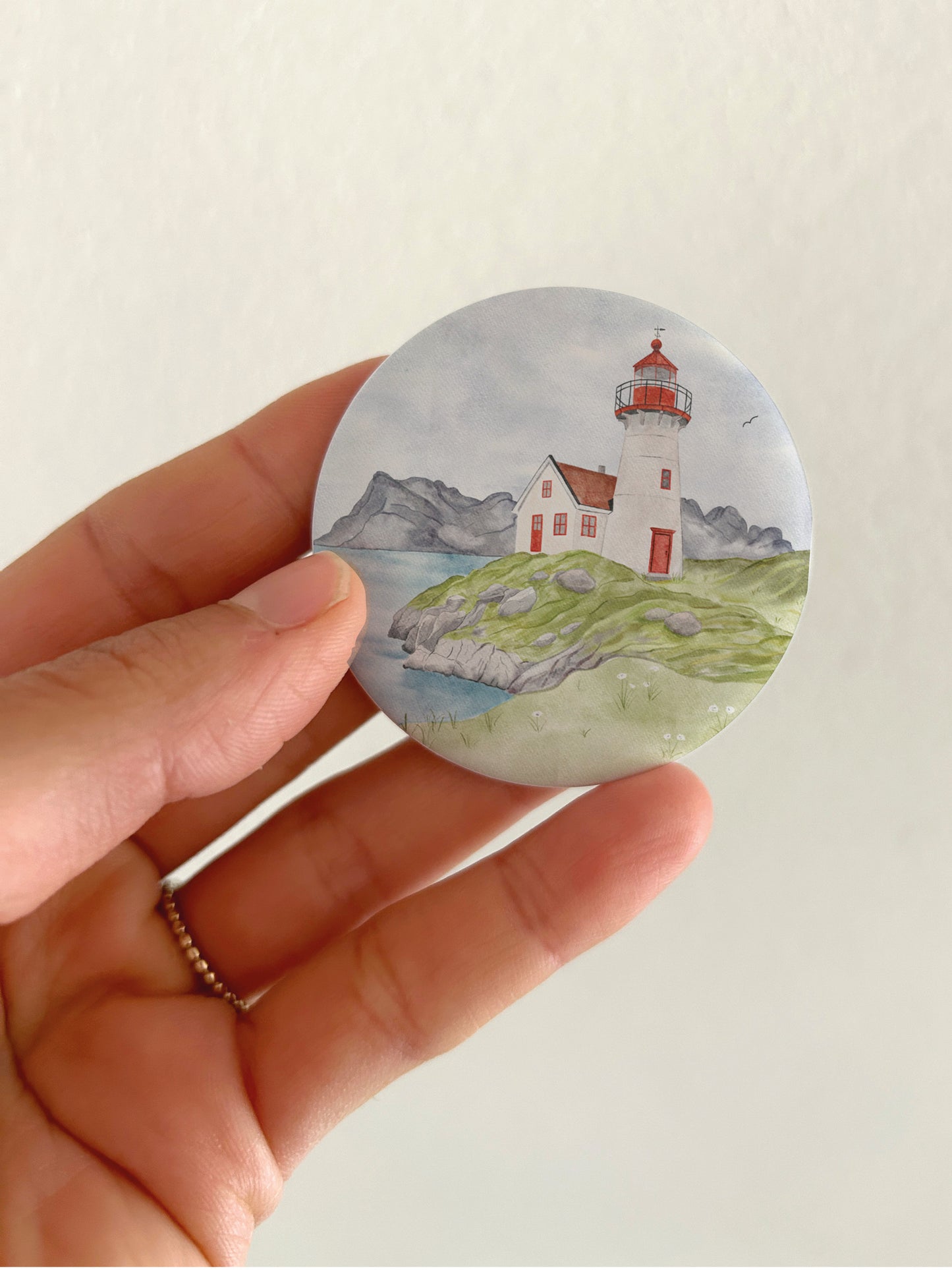 Großer maritimer Leuchtturm-Kühlschrankmagnet mit 55mm Durchmesser als Zubehör und Deko für das Wohnmobil oder Vanlife. Eine Hand präsentiert den runden, matten Magneten vor einer hellen Zimmerwand, um das reflexionsfreie Oberflächenfinish und die reale Produktgröße zu zeigen.