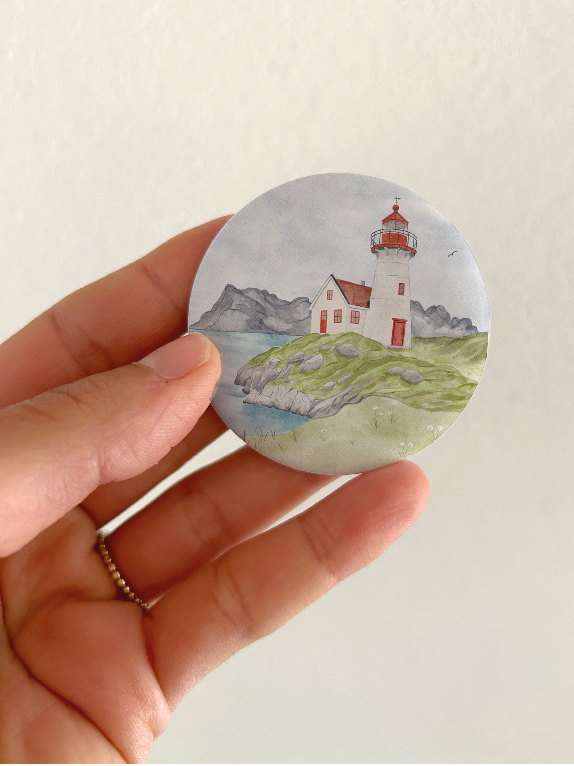 Großer maritimer Leuchtturm-Kühlschrankmagnet mit 55mm Durchmesser als Zubehör und Deko für das Wohnmobil oder Vanlife. Eine Hand präsentiert den runden, matten Magneten vor einer hellen Zimmerwand, um das reflexionsfreie Oberflächenfinish und die reale Produktgröße zu zeigen.