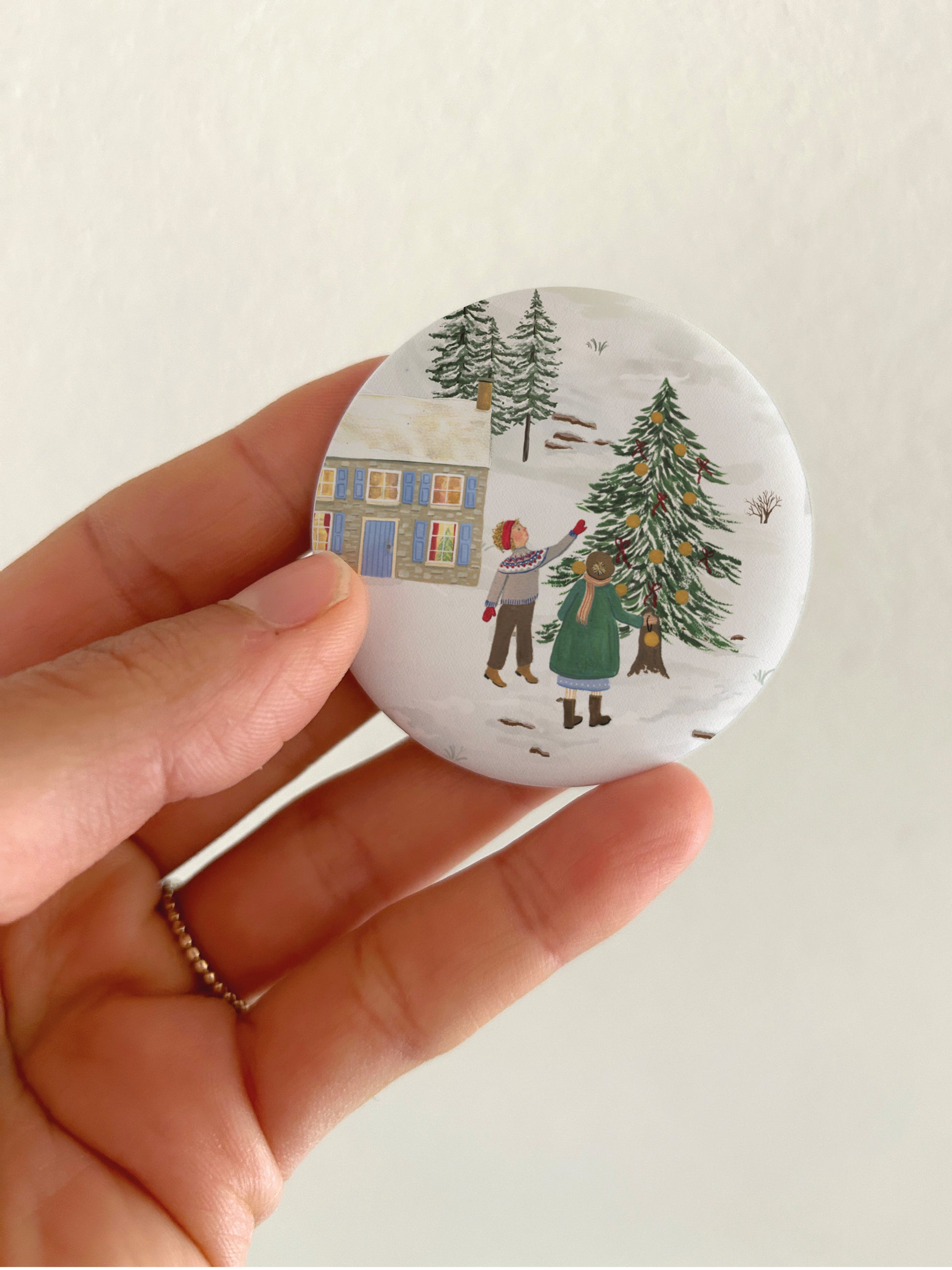 Großer Weihnachts-Magnet mit winterlicher Familienszene und 55mm Durchmesser als Dekoration für die Kühlschranktür. Ein runder, matter Magnet mit handgemalter Natur-Illustration aus Große-Magnete-Weihnachten3.jpg wird als Größenvergleich vor einem hellen Hintergrund in einer Hand gehalten, um die matte, kratzfeste und spiegelungsfreie Oberfläche zu präsentieren.