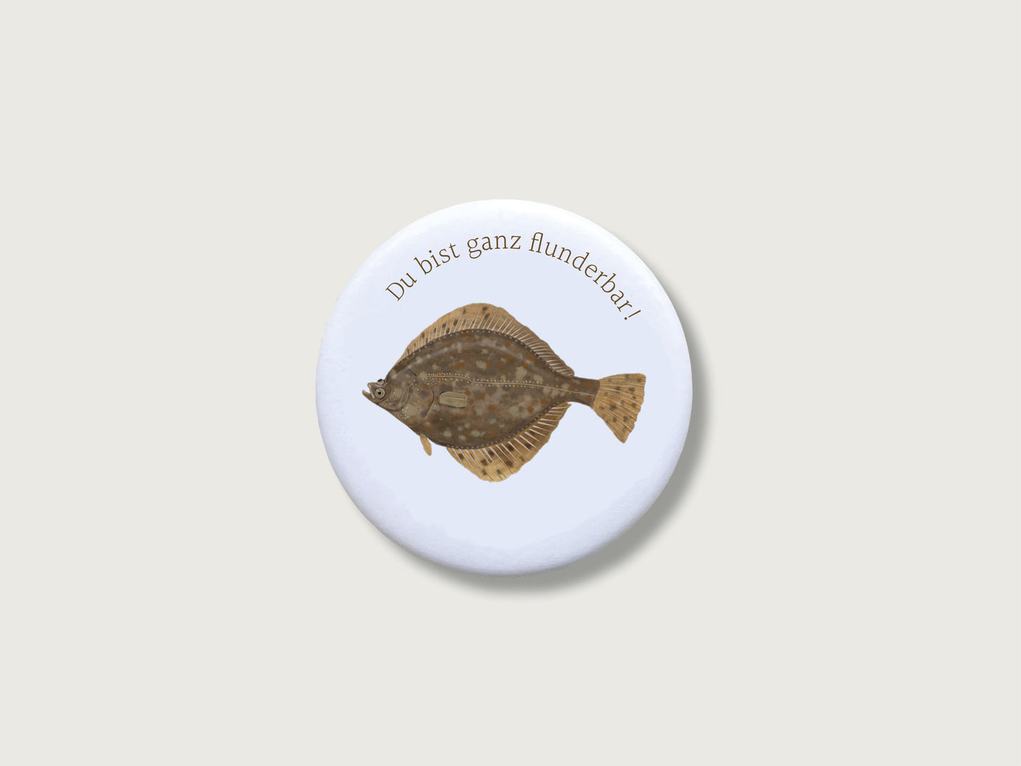 Runder, kratzfest versiegelter Button-Magnet mit 55 mm Durchmesser im matten Look. Zu sehen ist eine naturgetreue, illustrierte Plattfisch-Zeichnung (Flunder) mit einem humorvollen Wortspiel im modernen Country-Stil.