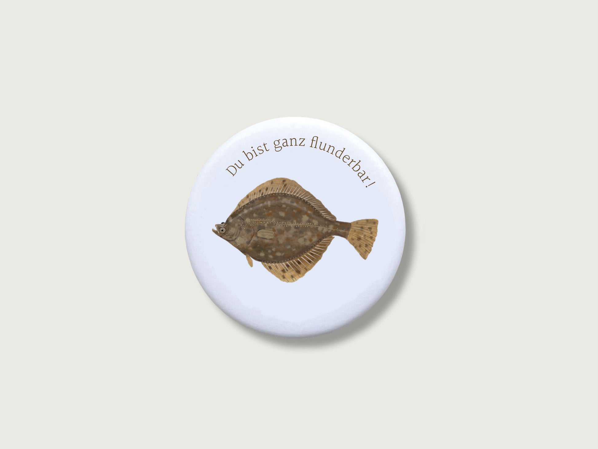 Runder, kratzfest versiegelter Button-Magnet mit 55 mm Durchmesser im matten Look. Zu sehen ist eine naturgetreue, illustrierte Plattfisch-Zeichnung (Flunder) mit einem humorvollen Wortspiel im modernen Country-Stil.