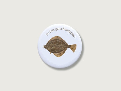 Runder, kratzfest versiegelter Button-Magnet mit 55 mm Durchmesser im matten Look. Zu sehen ist eine naturgetreue, illustrierte Plattfisch-Zeichnung (Flunder) mit einem humorvollen Wortspiel im modernen Country-Stil.