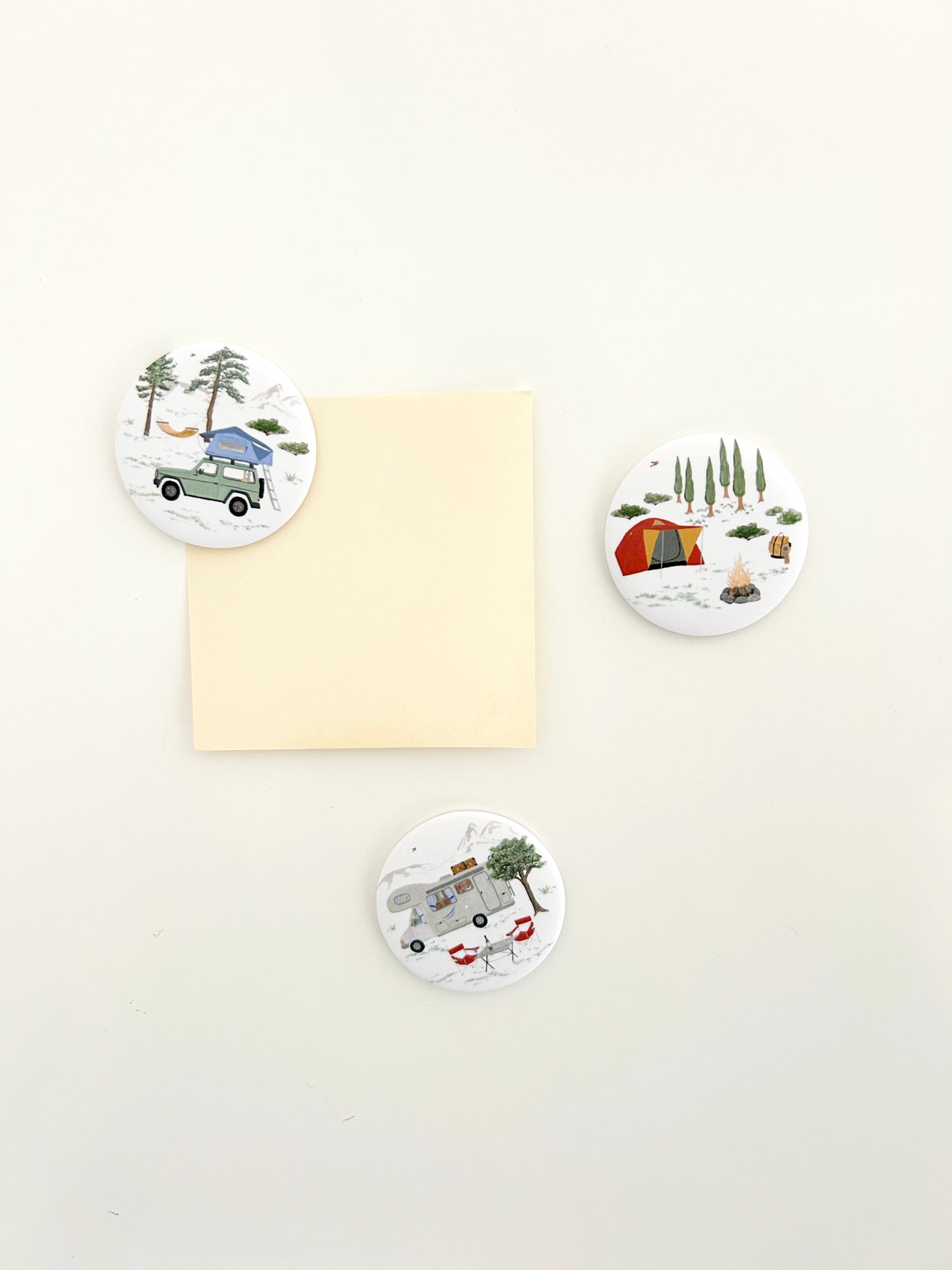 3 runde Magnete mit Campingmotiven an einer Magnetwand. Die großen Magnete Buttons zeigen Wohnmobil, Zelt und Jeep mit Dachzelt 