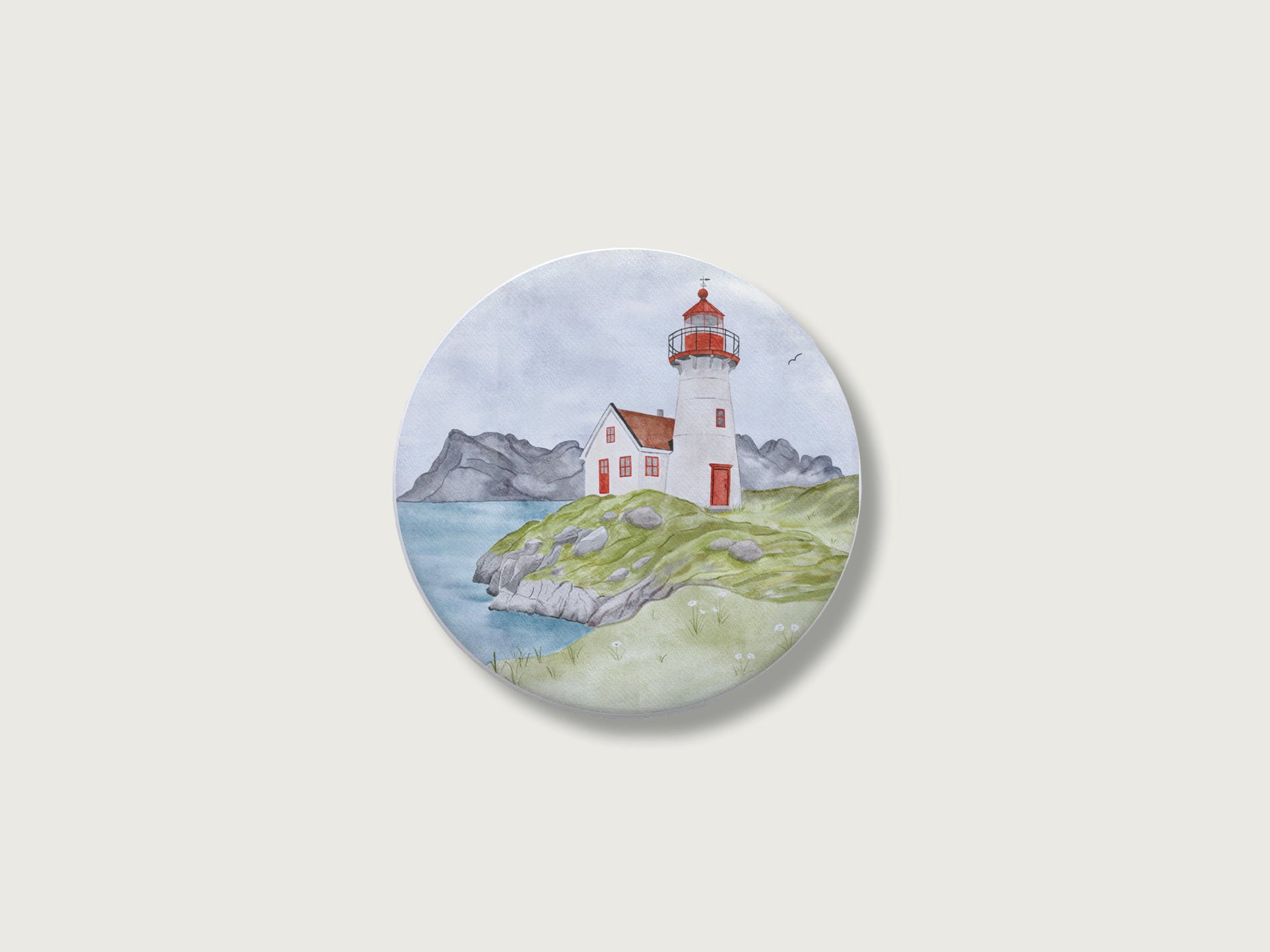 Maritimes Geschenk für Küstenkinder und Camper: Runder Kühlschrankmagnet mit einer malerischen, detailreichen Handillustration eines klassischen rot-weißen Leuchtturms und Wärterhäuschens auf einer grünen, felsigen Klippe direkt am Meer vor einer weiten Bergkulisse im Hintergrund.