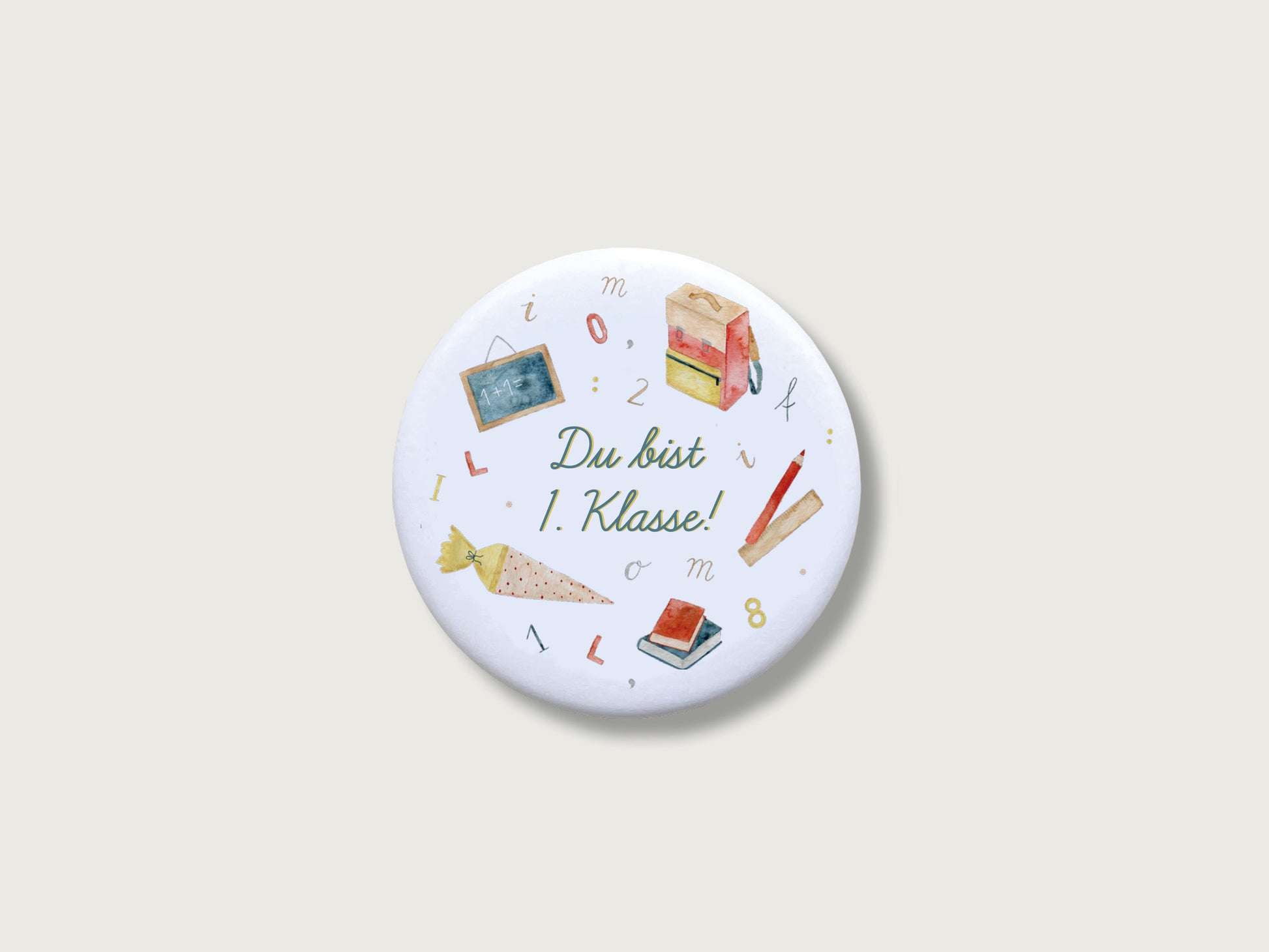 Runder, weißer Magnet, auf dem "Du bist 1. Klasse" steht und verschiedene passende Illustrationen, wie Schultüte, Büchertasche, Stift, Lineal und Bücher drumherum arrangiert sind. Die Motive wurden handgemalt.
