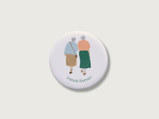 Persönliches Geschenk für die beste Freundin: Runder, weißer Kühlschrankmagnet mit Spruch Friends forever und einer handillustrierten Grafik von zwei älteren Frauen, die eng vertraut Arm in Arm von hinten zu sehen sind. Das Motiv im analogen Zeichenstil ist mittig auf einem schlichten, neutralen, hellen Hintergrund platziert.