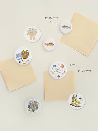 Magnetwand mit verschiedenen Magnetbuttons mit unterschiedlichen Motiven wie Muttertag für Mamas, Survival, Blumen, Wein und Käse oder Einschulung und Schulanfang.