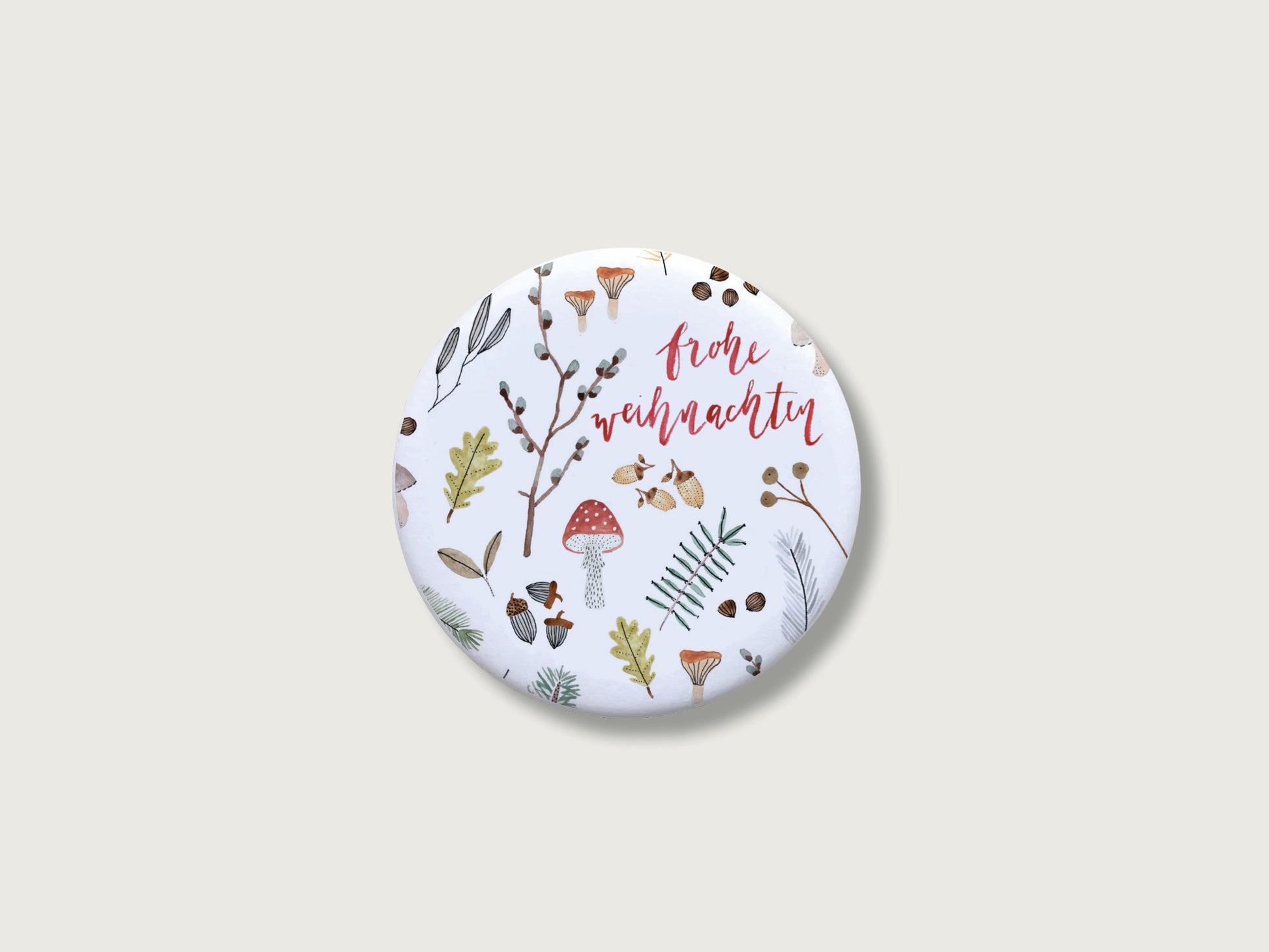 Botanische Weihnachtsdeko für die Küche: Runder, weißer Kühlschrankmagnet frohe weihnachten mit einer detailreichen, feinen Handillustration von verschiedenen Naturelementen aus dem Winterwald wie einem roten Fliegenpilz, grünen Tannenzweigen, kleinen Eicheln, Blättern und Zapfen auf einem schlichten, hellen Hintergrund.