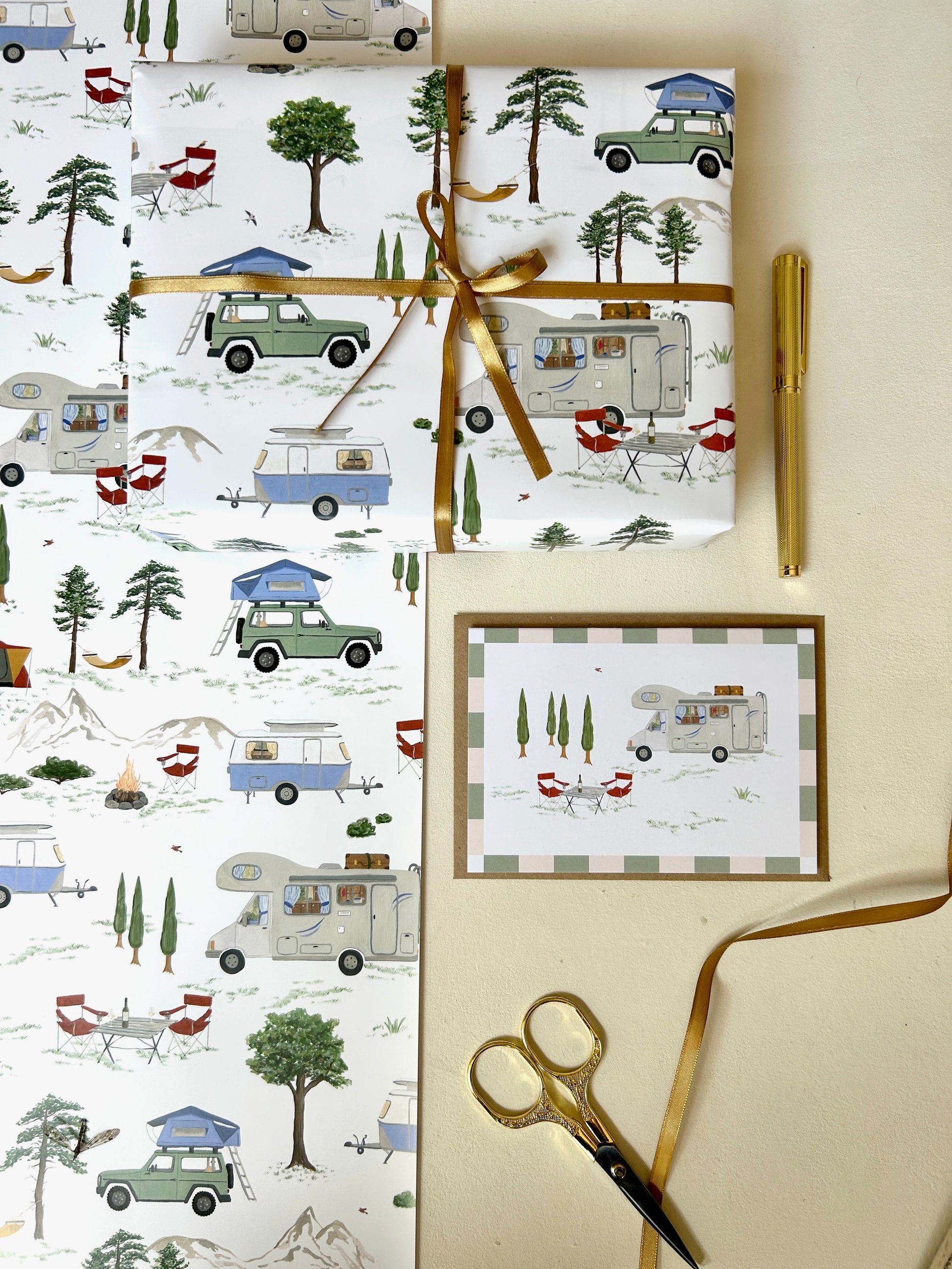 Geschenkverpackung im Camping-Stil: Hochwertiges Geschenkpapier in Bögen, ein verpacktes Präsent mit Goldschleife und eine passende Wohnmobil-Klappkarte mit Umschlag. Das Geschenkpapier zeigt ein Camper Motiv mit Wohnwagen, Wohnmobil und Offraod-Fahrzeug mit Dachzelt in einer natürlichen Camping-Kulisse. 