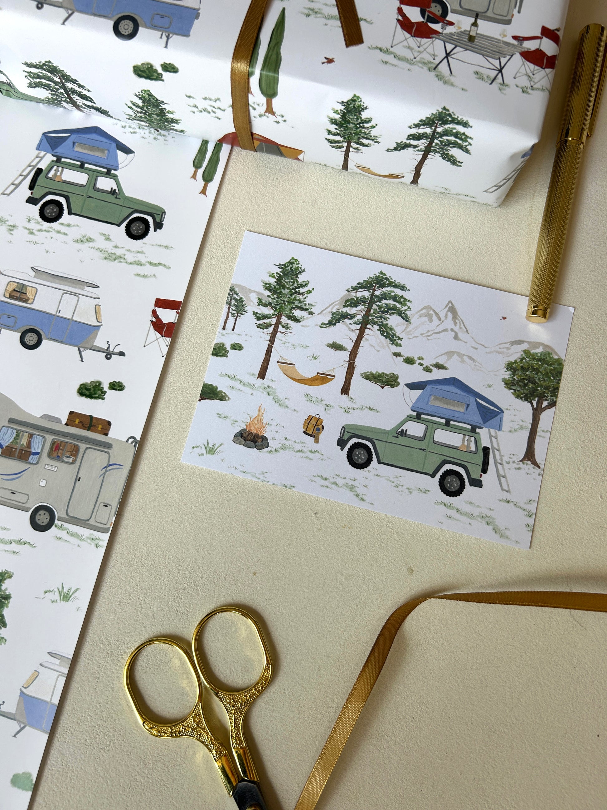 Kunstvolle Camping-Postkarte mit handgemalter Illustration eines Geländewagens mit Dachzelt, Lagerfeuer und Hängematte, arrangiert mit passendem Geschenkpapier.