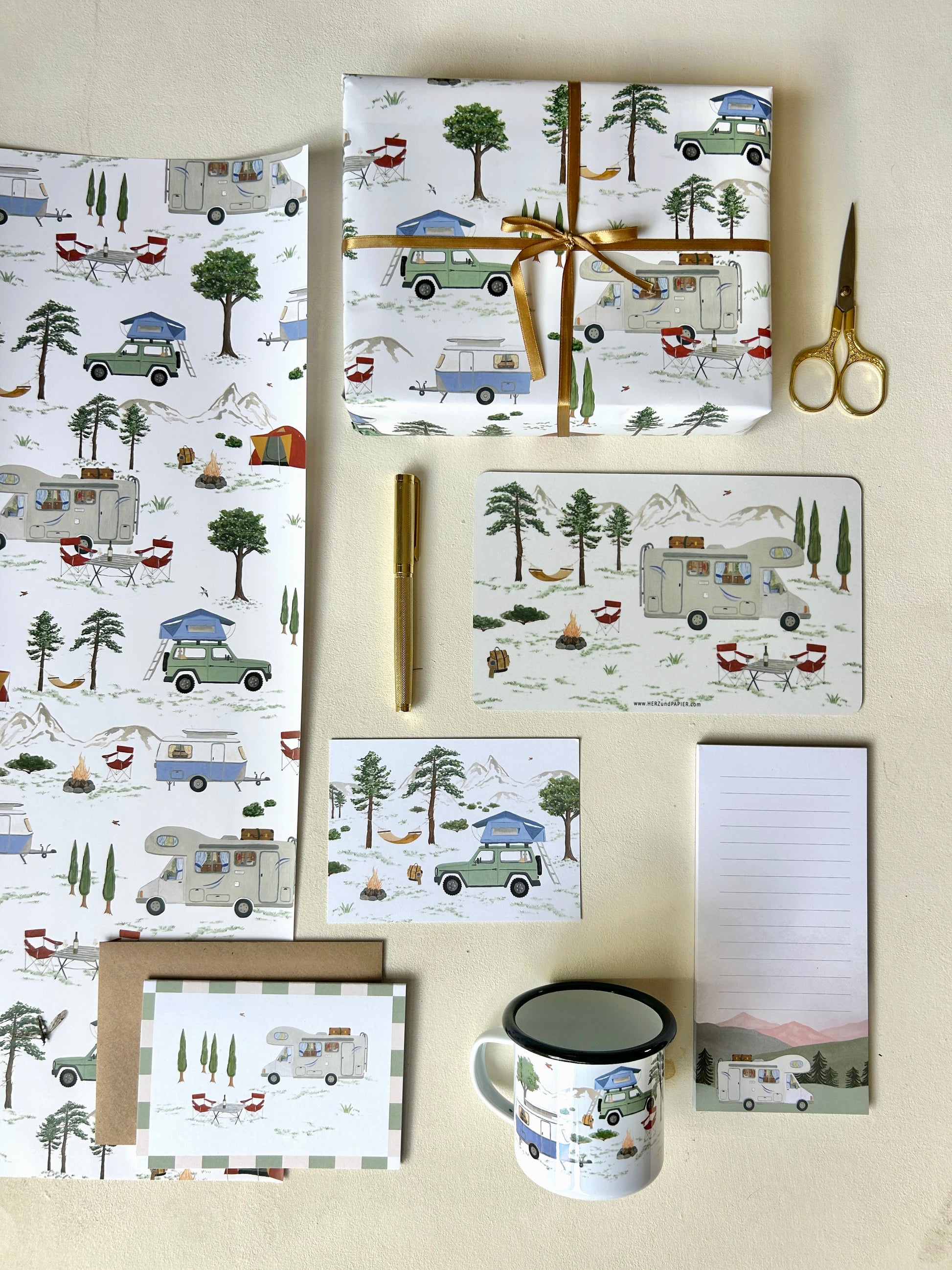 Ganzheitliche Produktübersicht der Camping- und Vanlife-Kollektion: Melamin-Frühstücksbrettchen, Emaille-Tasse, Geschenkpapier in Bögen, Notizblock und kunstvolle Postkarten im Natur-Look. Alle Produkte zieren handgemalte Illustrationen von Camping-Szenen mit Wohnwagen, Wohnmobil und Dachzelt sowie Zelten.