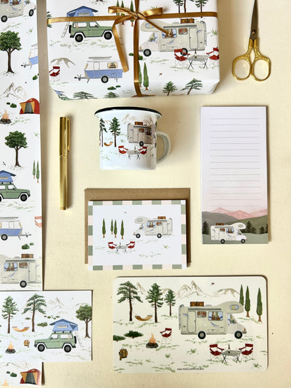 Camping-Geschenke und Papeterie-Kollektion im Flatlay: Nachhaltiges Geschenkpapier, Postkarten, Notizblock und Emaille-Tasse mit handgemalten Wohnmobil-, Wohnwagen-, Dachzelt- und Outdoor-Illustrationen. Die Illustrationen zeigen ein Allover, wiederkehrendes Camping-Motiv mit verschiedenen Fahzeugen in der Natur zwischen Bergen und Bäumnen.