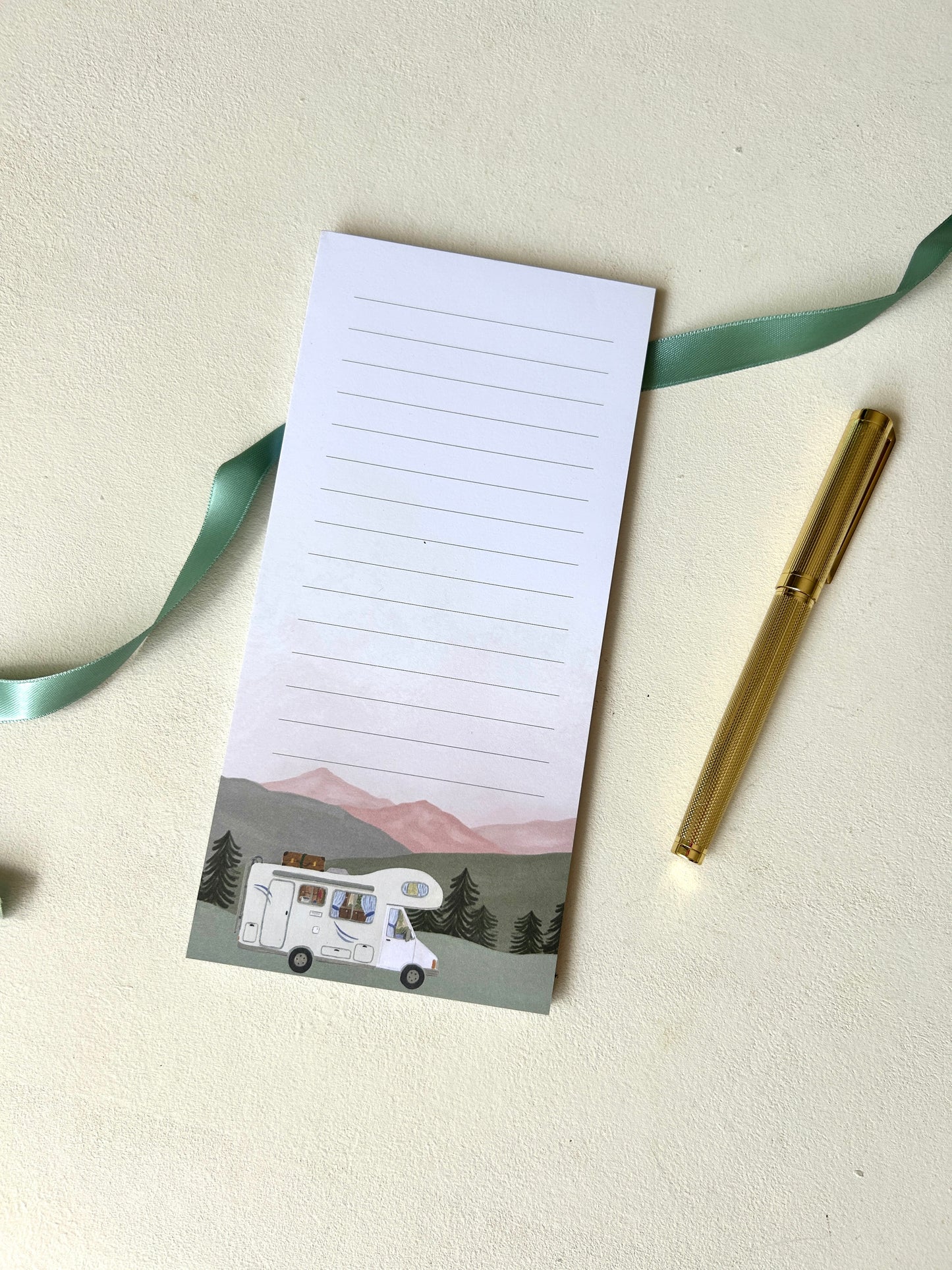 Linierter Notizblock im Camping-Design mit handgemalter Aquarell-Illustration eines Wohnmobils vor einer Bergkulisse, elegant dekoriert mit goldenem Stift.