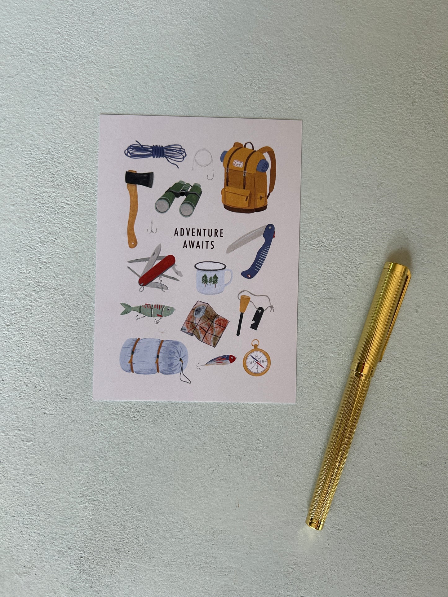 Eine illustrierte Postkarte mit dem Schriftzug „ADVENTURE AWAITS“ liegt auf einem hellgrauen, strukturierten Hintergrund. Auf der Karte sind detailreiche, handgemalte Survival-Motive wie ein Rucksack, Fernglas, Kompass, Taschenmesser und ein Zelt zu sehen. Rechts daneben liegt ein edler, goldener Füllfederhalter. Eine Karte, die an Wandern, Survival oder Bushcraft erinnert. 
Handgemalte, bunte Illutrationen. 