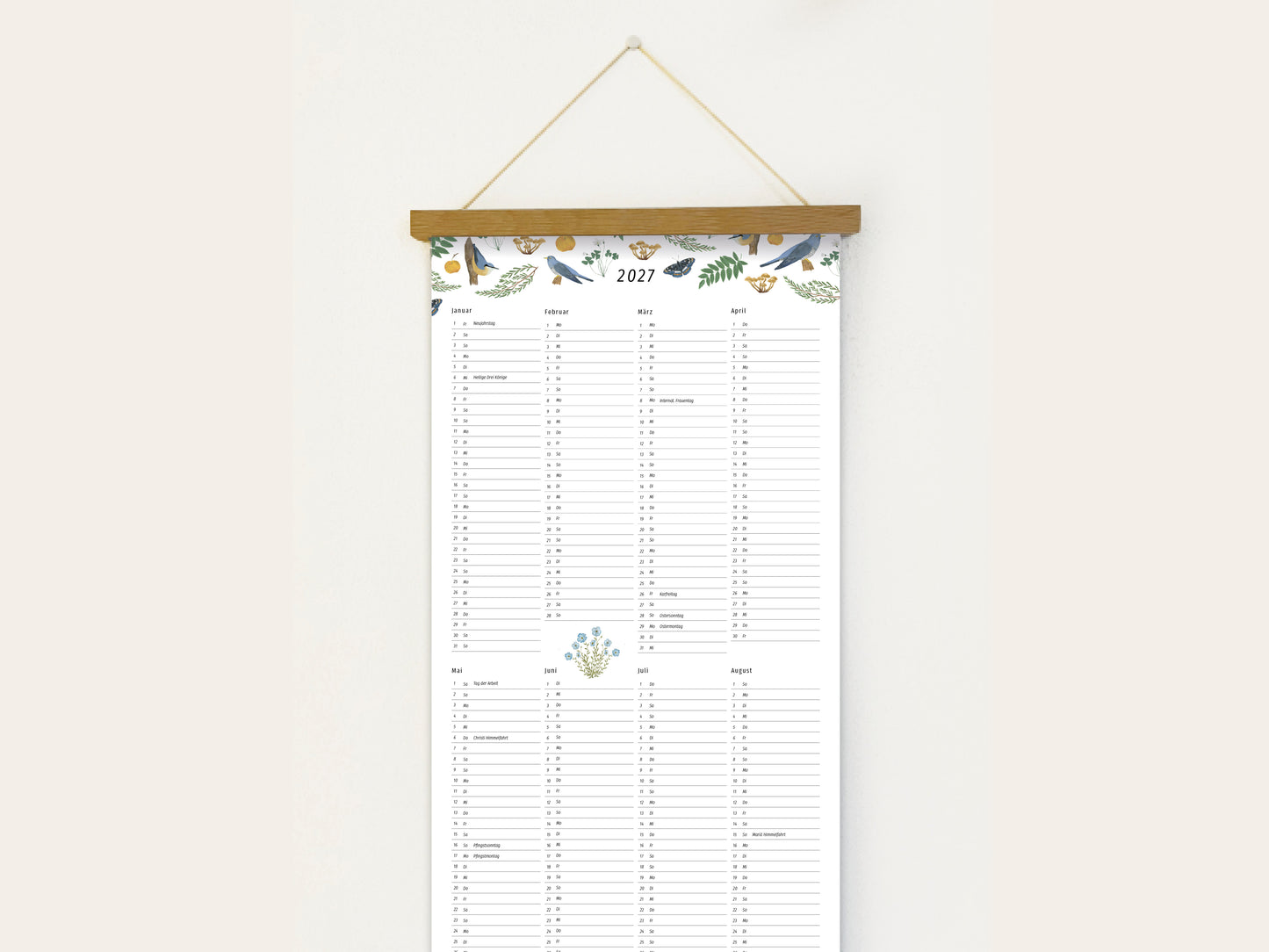 Langformatiger Wandplaner 2027 mit handillustrierten Vögeln, Schmetterlingen und botanischen Aquarell-Motiven, aufgehängt an einer Holzleiste vor einer weißen Wand.