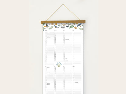 Langformatiger Wandplaner 2027 mit handillustrierten Vögeln, Schmetterlingen und botanischen Aquarell-Motiven, aufgehängt an einer Holzleiste vor einer weißen Wand.