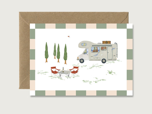 Klappkarte in weiß mit braunem Kraft-Papier Umschlag. Auf der Klappkarte ist ein handillustriertes Wohnmobil-Motiv zu sehen. Das Womo mit Alkoven steht neben Zypressen, davor ist ein Campingtisch mit Campingstühlen aufgebaut. Um die Camping Illustration ist eine gestreifte Borte angebracht.