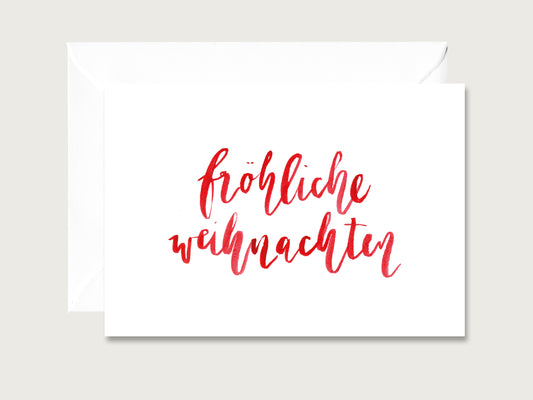 Klappkarte aus festem Naturpapier mit dem Schriftzug Froehliche Weihnachten in roter Pinselschrift neben passendem Umschlag.