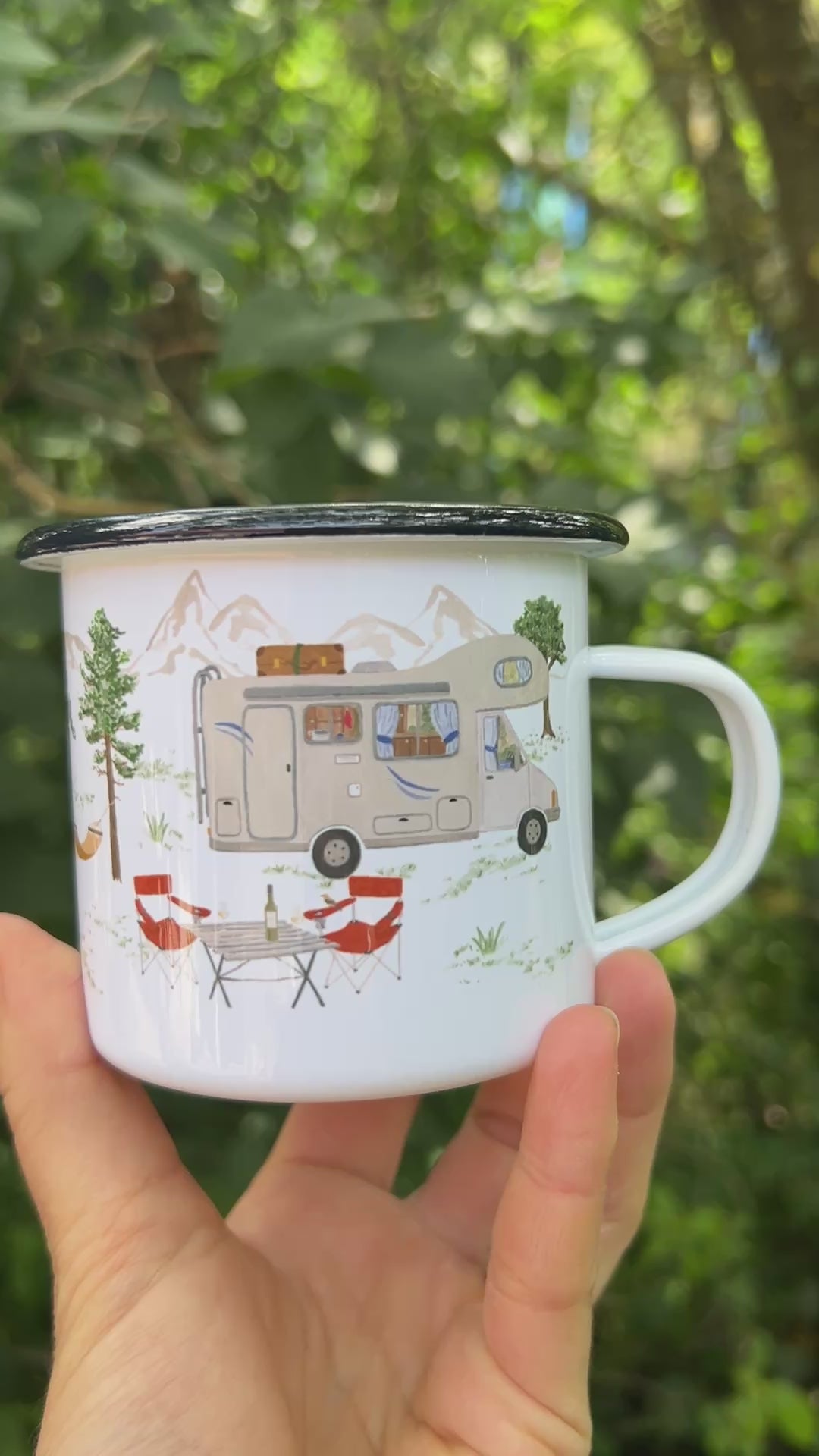 Eine Hand hält eine weiße Emaille-Tasse vor einem weich gezeichneten, grünen Waldhintergrund und dreht sie langsam um 360 Grad. Dabei wird das vollständige, umlaufende und detailreiche Design aus handgemalten Camping- und Naturmotiven wie Lagerfeuer, Rucksack, Bäumen und Outdoor-Ausrüstung sichtbar.
